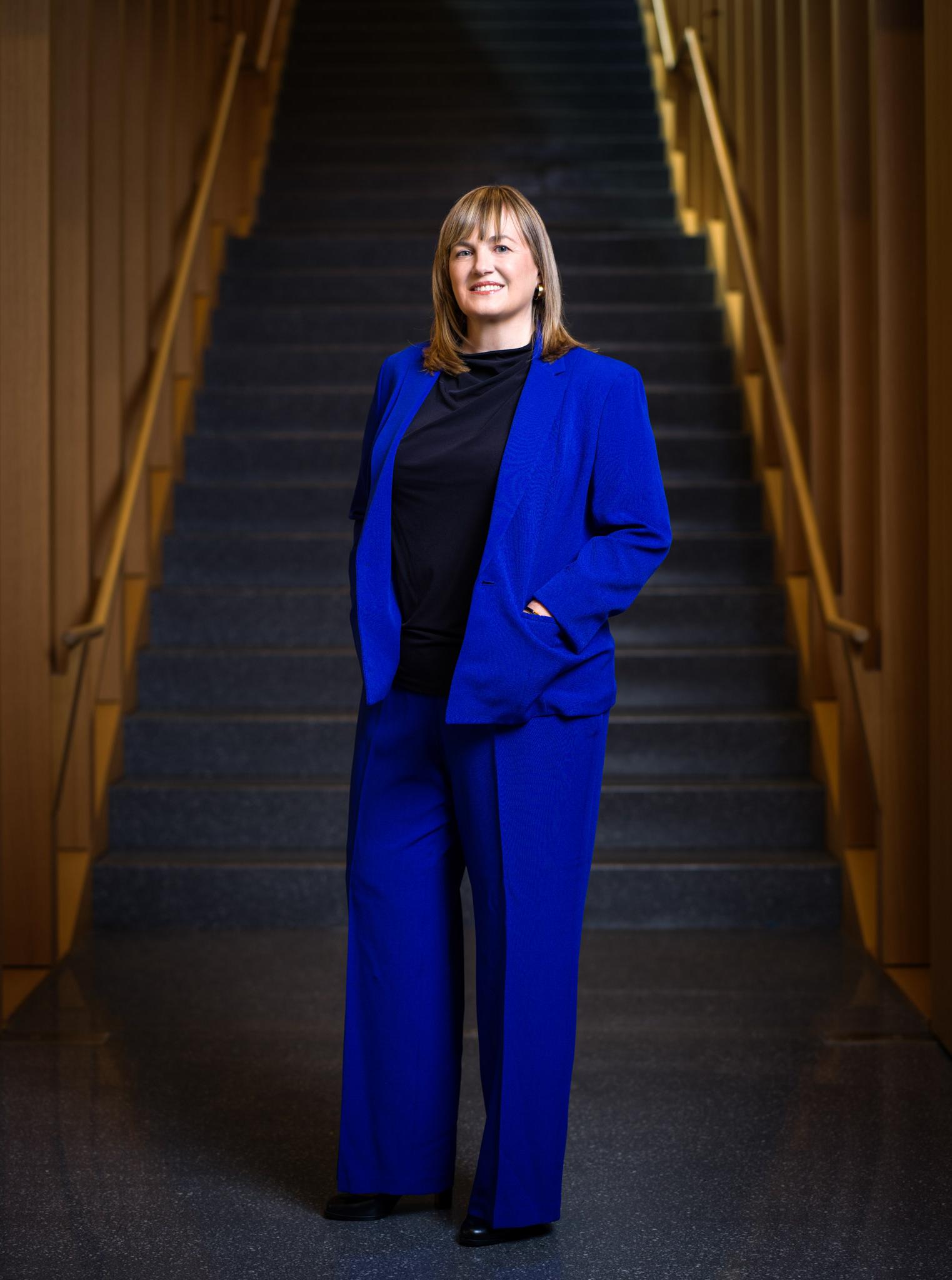 劳拉·罗森伯里总统站在米尔斯坦大楼的楼梯前. 她穿着一套蓝色的衣服